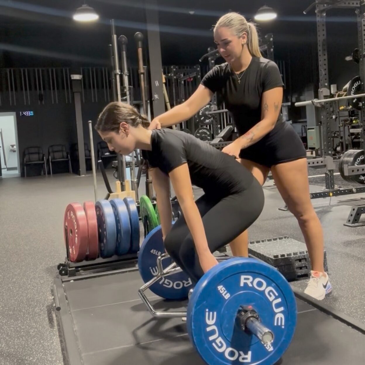 Coach Lexi setting a student-athlete's back angle at the bottom of a hex bar deadlift